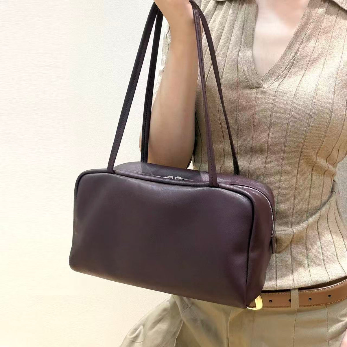 Vesper burgundy shoulder bag held by its twin straps against a neutral outfit